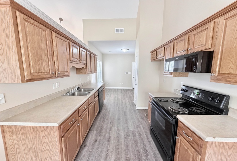 Galley kitchen featuring wood-finish cabinetry, light-toned countertops, a double-basin stainless steel sink, black range, and an over-the-range microwave