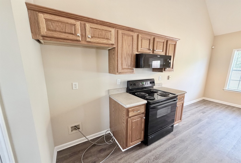 Kitchenette featuring wood-finish cabinetry, a built-in microwave, a black electric range, and laminate countertops