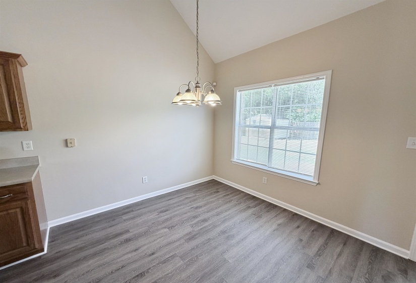 Open dining area featuring high vaulted ceilings, a large window with blinds, a multi-light chandelier, wood-finish flooring, and a built-in lower cabinet with a light-colored countertop