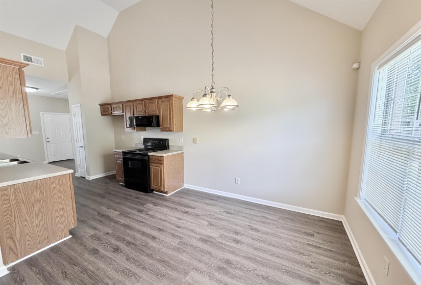 Kitchen area featuring wood-finish laminate flooring, vaulted ceilings, and a window with blinds