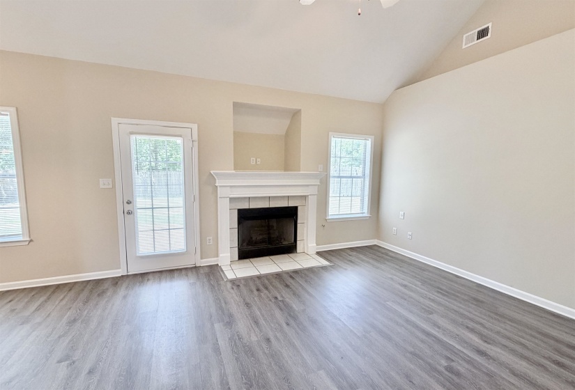 Living area featuring wood-finish flooring, a white-mantled fireplace with a tiled hearth, vaulted ceiling, and a glass-paned exterior door