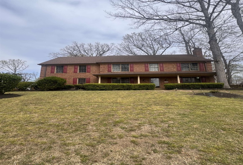 Brick exterior residence featuring a covered front porch with columns, a shingle roof, and mature perimeter trees