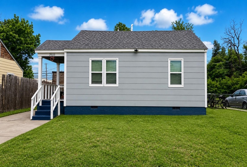 Single-story residence featuring light gray siding with white trim, a dark gray shingle roof, and a blue foundation