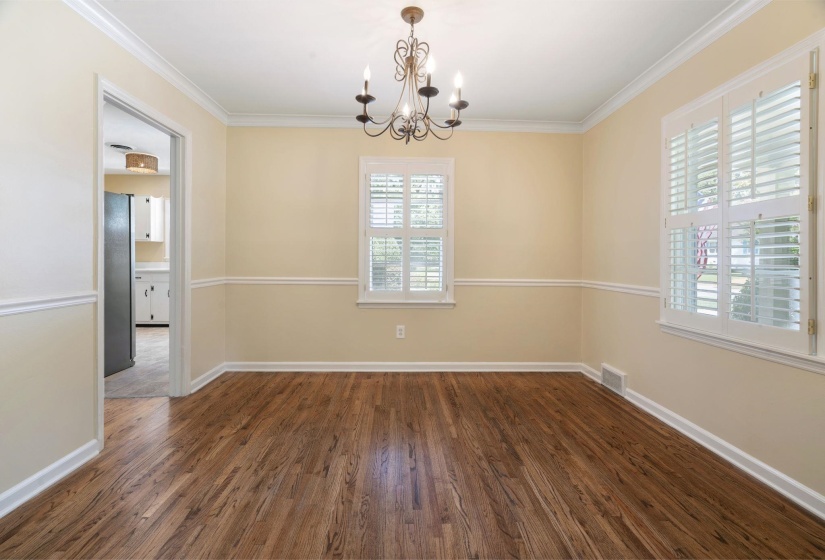 Room featuring beautiful hardwood flooring, white plantation shutters, crown molding, chair rail molding, and a lovely chandelier