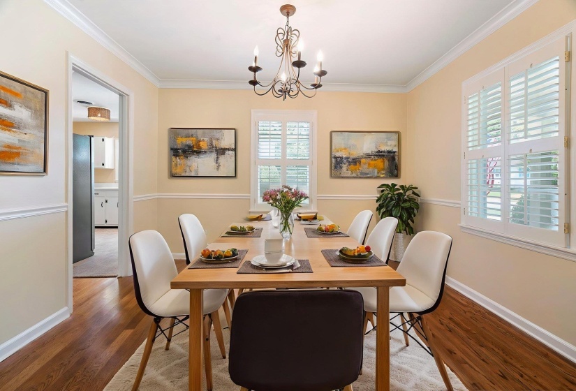 Room featuring beautiful hardwood flooring, white plantation shutters, crown molding, chair rail molding, and a lovely chandelier