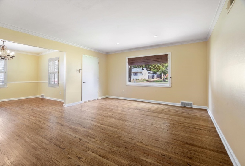 Spacious interior room featuring beautiful hardwood flooring, light neutral wall paint, and white crown molding