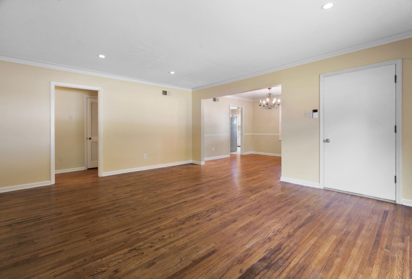 Spacious interior room featuring beautiful hardwood flooring, light neutral wall paint, and white crown molding
