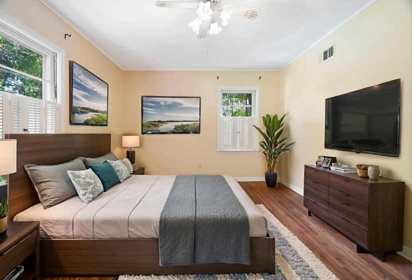 Bedroom featuring wood-finish flooring, two windows with white shutters, crown molding, and a ceiling fan with integrated lighting