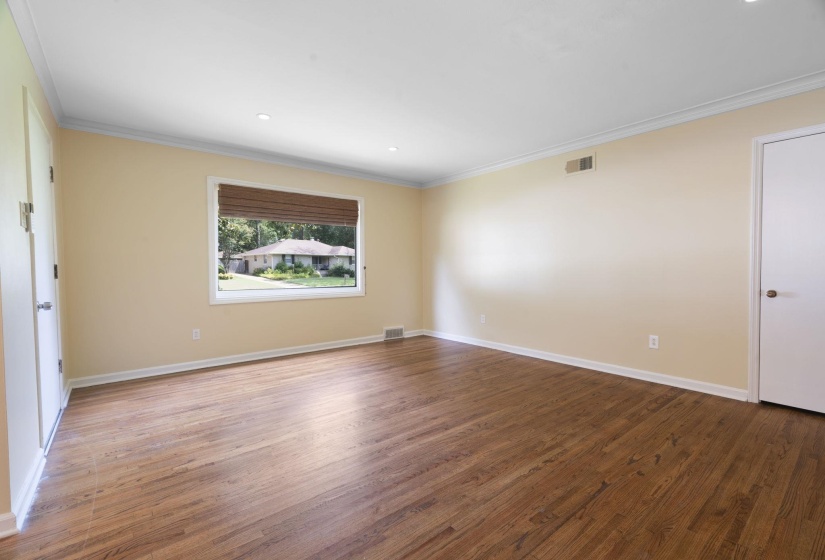 Spacious interior room featuring beautiful hardwood flooring, light neutral wall paint, and white crown molding