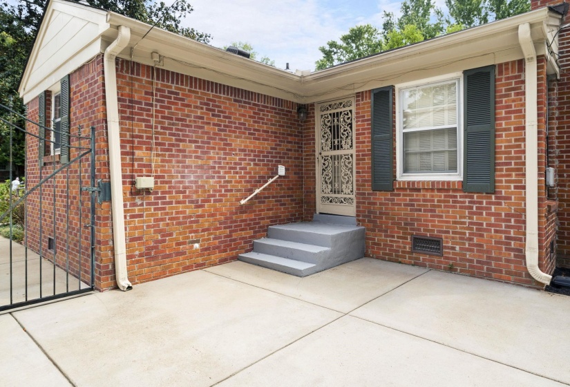Brick exterior featuring a decorative iron door, exterior steps with a handrail, and a concrete patio
