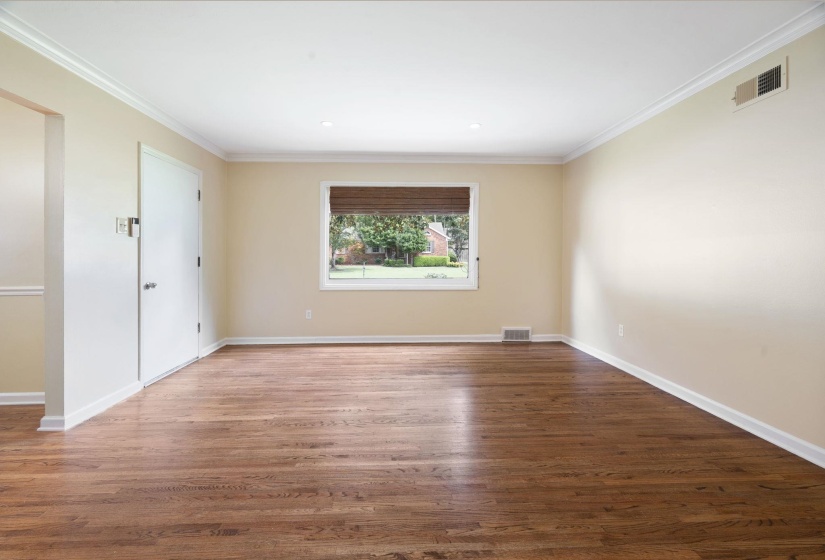 Spacious interior room featuring beautiful hardwood flooring, light neutral wall paint, and white crown molding