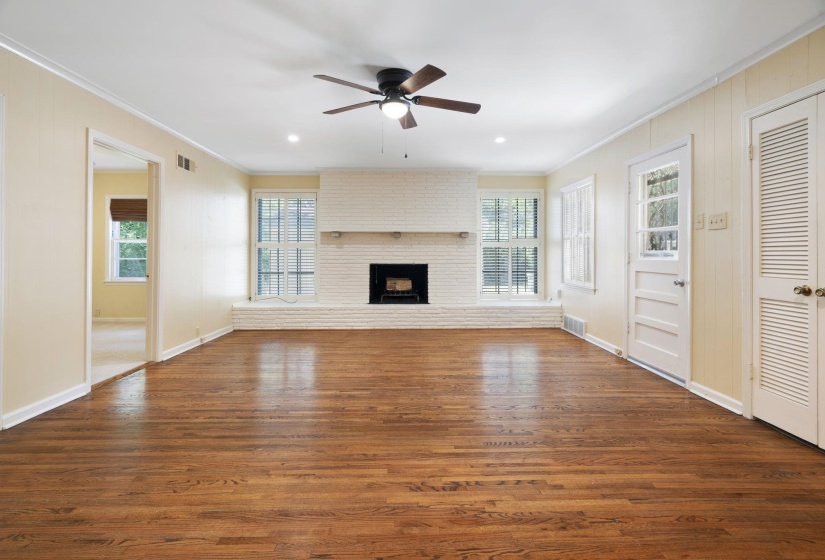 Large living area featuring beautiful hardwood flooring, a white brick fireplace with a mantel, multiple windows with blinds, recessed lighting, and a ceiling fan