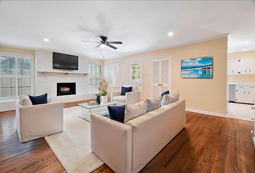 Large living area featuring beautiful hardwood flooring, a white brick fireplace with a mantel, multiple windows with blinds, recessed lighting, and a ceiling fan