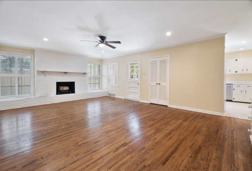 Large living area featuring beautiful hardwood flooring, a white brick fireplace with a mantel, multiple windows with blinds, recessed lighting, and a ceiling fan