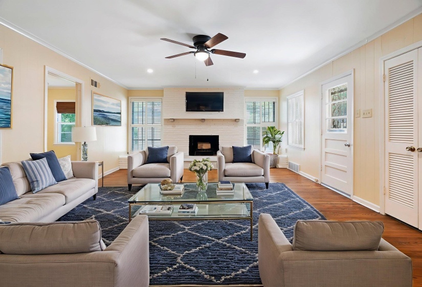 Large living area featuring beautiful hardwood flooring, a white brick fireplace with a mantel, multiple windows with blinds, recessed lighting, and a ceiling fan