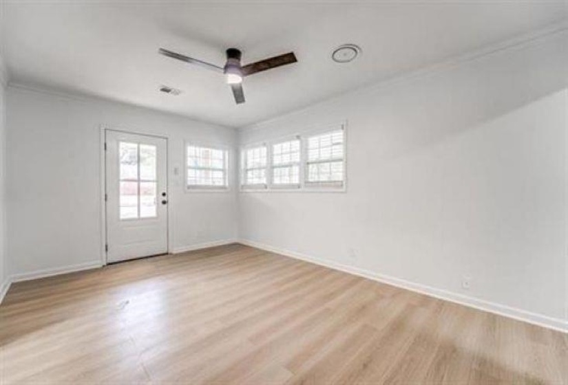 Bright interior space featuring a glass-paneled door, multiple windows with white blinds, light wood-finish flooring, a ceiling fan, and white baseboards