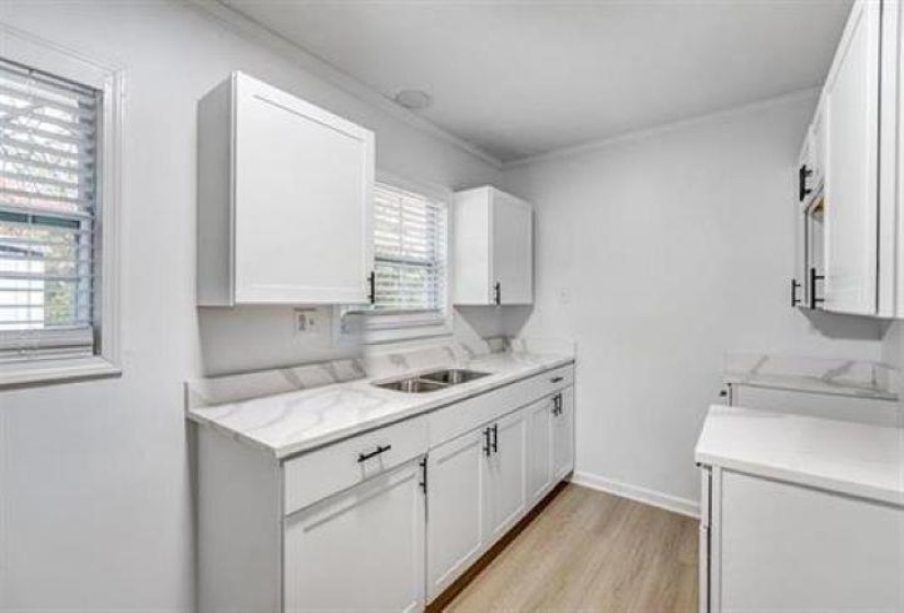 Modern kitchen featuring white shaker cabinetry, brushed black hardware, wood-finish flooring, and light-toned countertops with a subtle gray veining