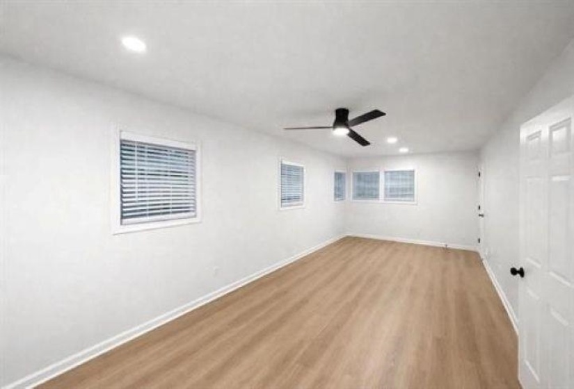 Spacious room featuring wood-finish flooring, multiple windows with blinds, recessed lighting, a ceiling fan, and white baseboards