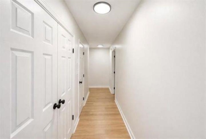 Hallway featuring light wood-finish flooring and multiple paneled doors with black hardware