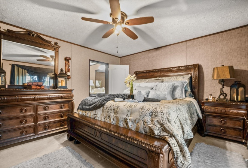 Spacious bedroom featuring textured wall finishes, a ceiling fan with integrated lighting, and carpeted flooring