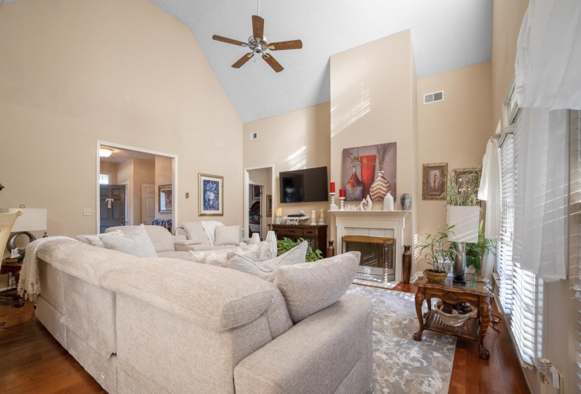 Spacious living area featuring a vaulted ceiling with a ceiling fan, hardwood flooring, and a fireplace with a mantel