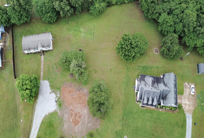 Expansive lot featuring a primary residence with a multi-gable roof, a separate auxiliary structure, mature trees, a gravel driveway, and a paved driveway