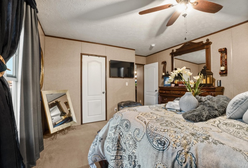Bedroom featuring a ceiling fan with integrated lighting, textured walls, two paneled doors, and wood-finish trim