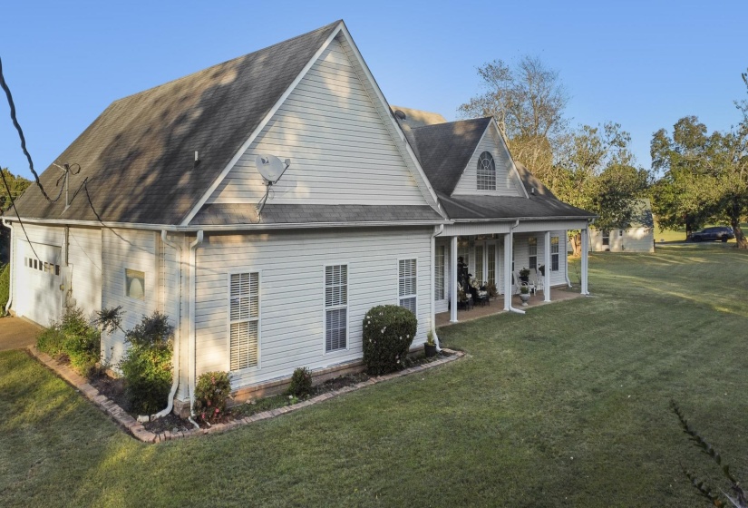 Exterior featuring white siding, a covered porch, a prominent dormer with an arched window, an attached garage with a panel door, and a manicured lawn