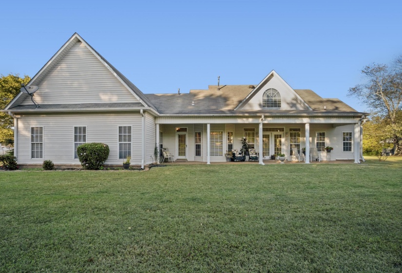 Expansive rear yard featuring a large covered patio with substantial columns, multiple exterior entry points, and a prominent arched window on the upper level