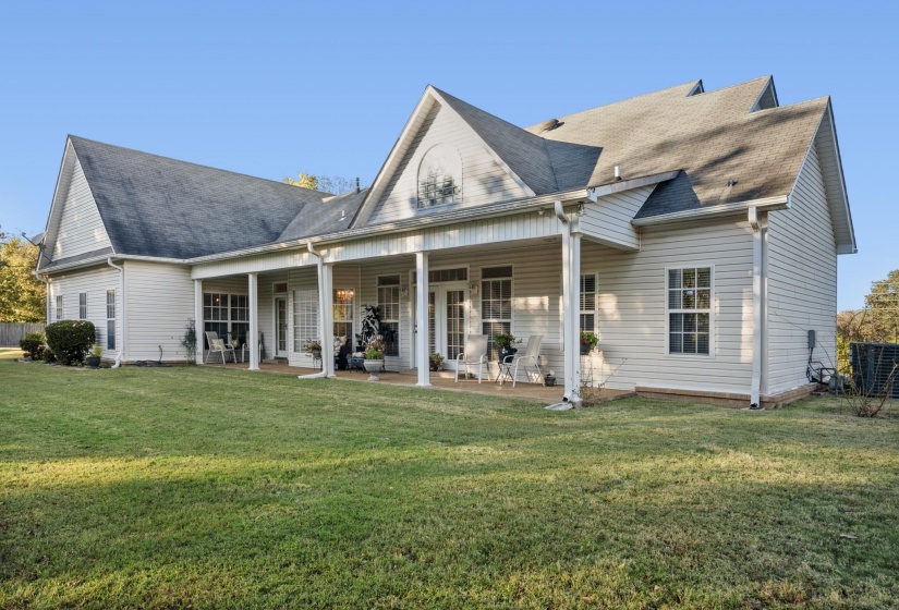 Expansive rear exterior featuring a covered porch, white vinyl siding, multiple windows, and a generous green lawn