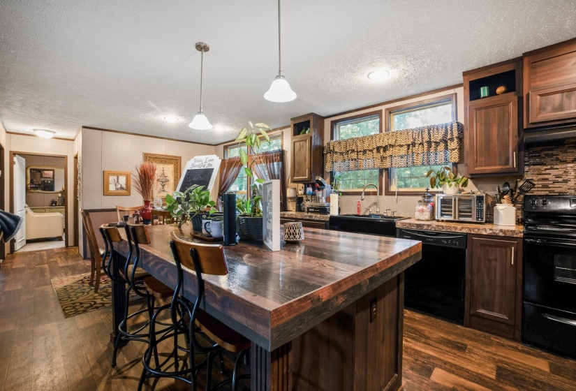 Kitchen featuring a spacious island with wood-finish countertop, pendant lighting, wood-finish flooring, dark wood cabinetry, and a black appliance suite