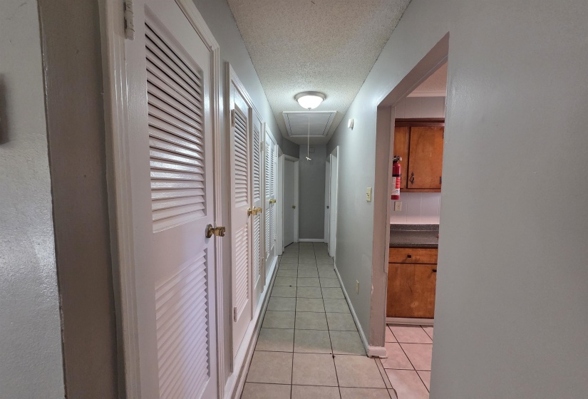 Hallway featuring attic access, light tile patterned floors, and a textured ceiling
