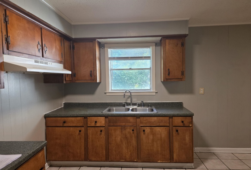 Kitchen with dark countertops, light tile patterned floors, ornamental molding, under cabinet range hood, and brown cabinetry