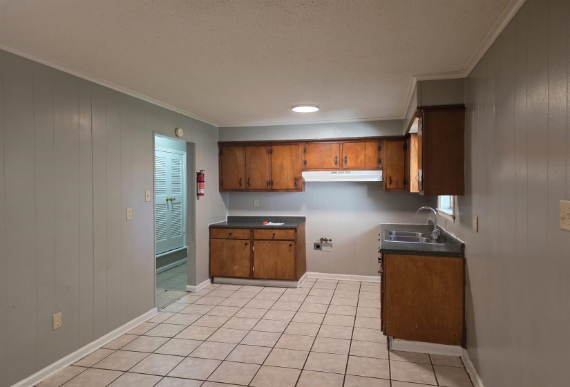 Kitchen featuring wooden walls, dark countertops, brown cabinets, crown molding, and light tile patterned floors