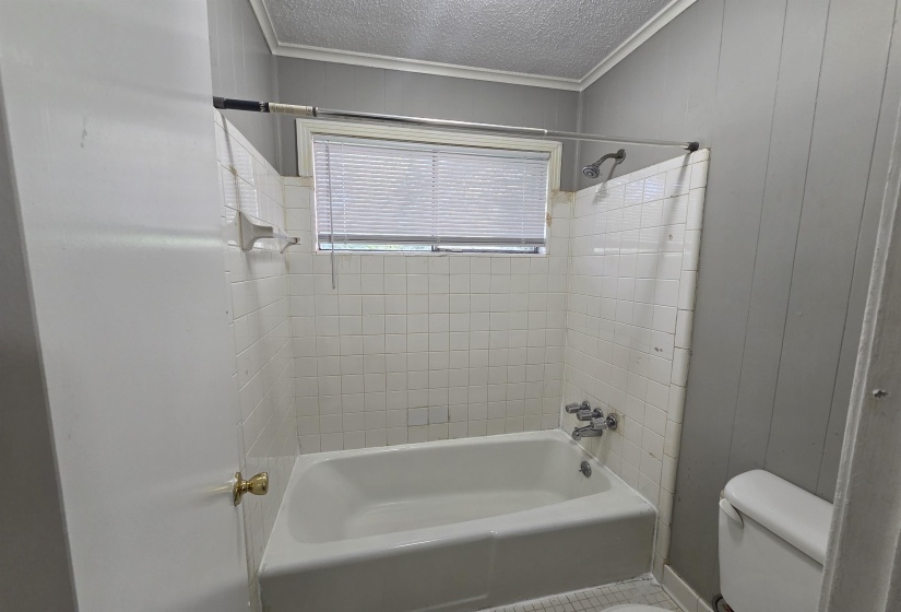 Bathroom featuring crown molding, washtub / shower combination, a textured ceiling, and wood walls