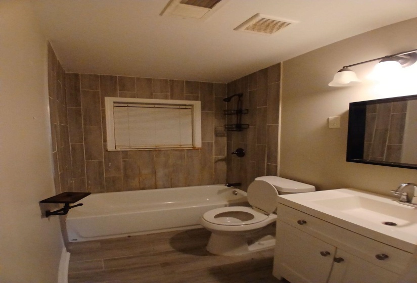 Bathroom featuring wood-look tile flooring, a white tub with tile surround, and a vanity with a white integrated sink