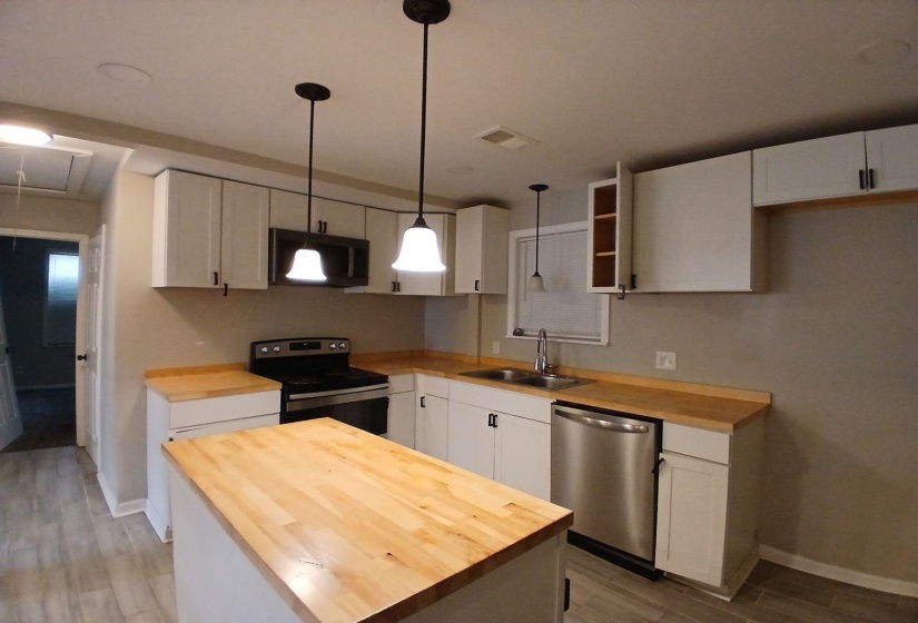 Kitchen featuring an island with wood-finish countertop, light-toned cabinetry with dark hardware, stainless steel appliances, and tile flooring