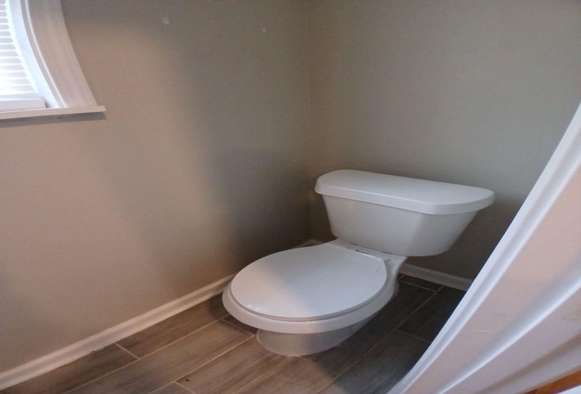 Powder room featuring a white toilet, neutral wall paint, and wood-finish tile flooring