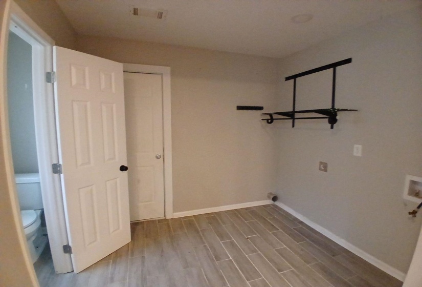 Utility room featuring wood-finish tile flooring, light neutral wall paint, and a wall-mounted black metal shelving unit