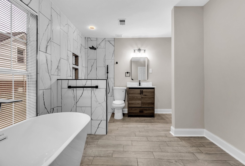 Bathroom featuring vanity, a marble finish shower, tile walls, a freestanding tub, and wood finish floors