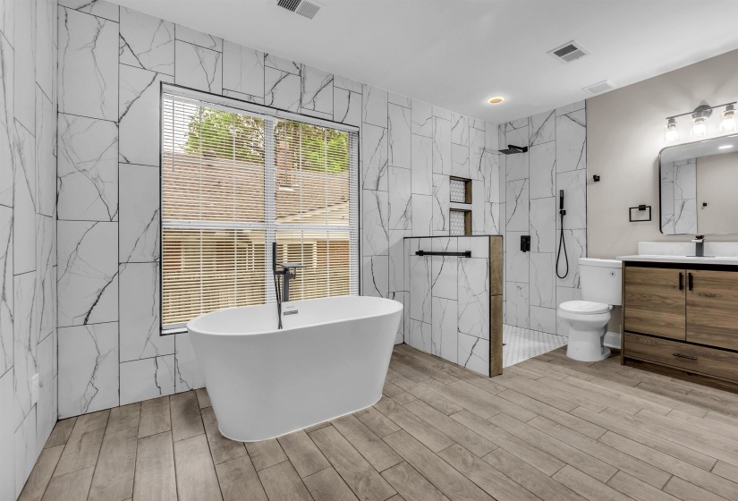 Full bathroom with a marble finish shower, vanity, a freestanding bath, wood finish floors, and tile walls