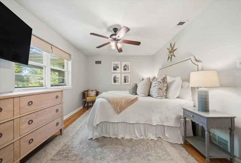 Bedroom featuring wood-finish flooring, a contemporary ceiling fan, and a light-toned upholstered headboard