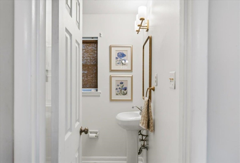 Pedestal sink with polished chrome fixtures, framed mirror, and wall-mounted sconce