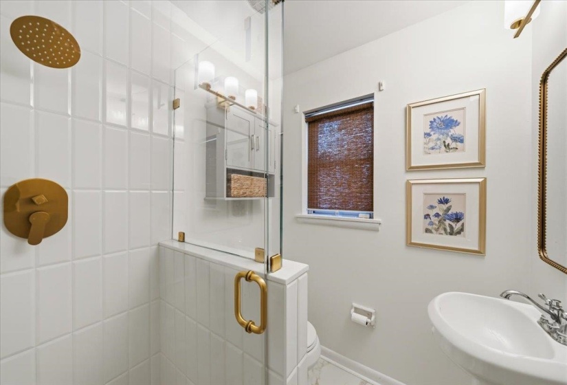 Shower with glass enclosure, featuring gold-toned fixtures and white subway tile
