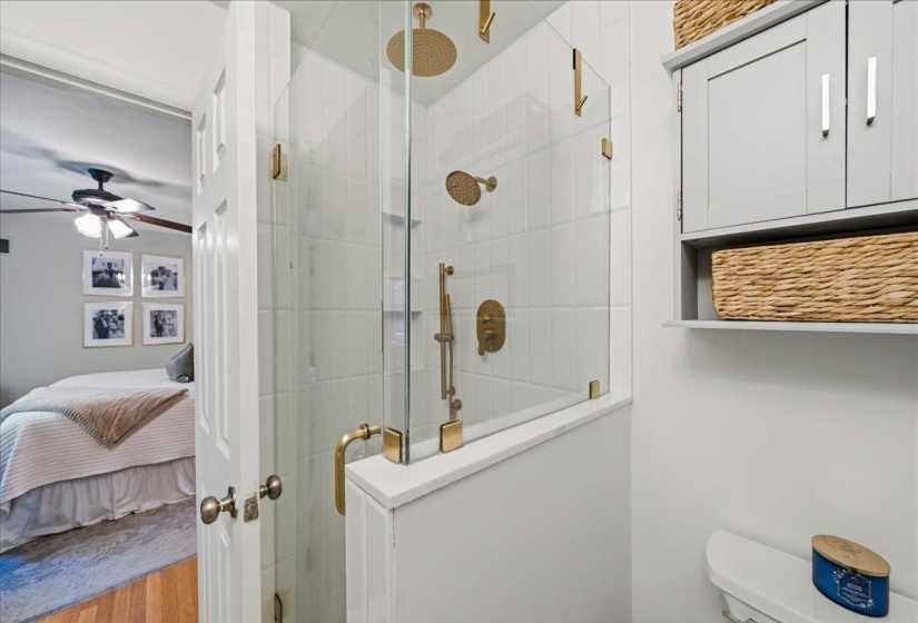 Frameless glass shower enclosure with brass fixtures, including a rainfall showerhead and handheld sprayer