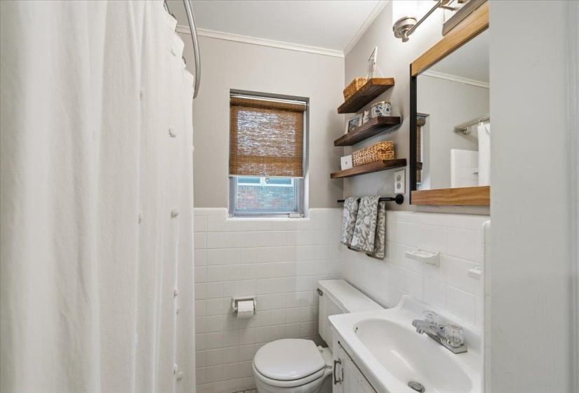 Bathroom featuring white tile wainscoting and a framed mirror with wood-finish accents