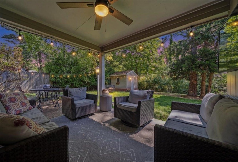 Covered patio featuring string lighting, a ceiling fan, concrete flooring, and a shed in the background