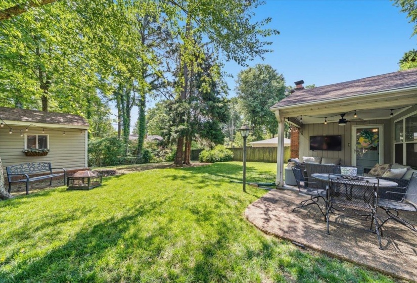 Manicured lawn with a spacious patio, covered outdoor living area, detached storage shed, and mature trees