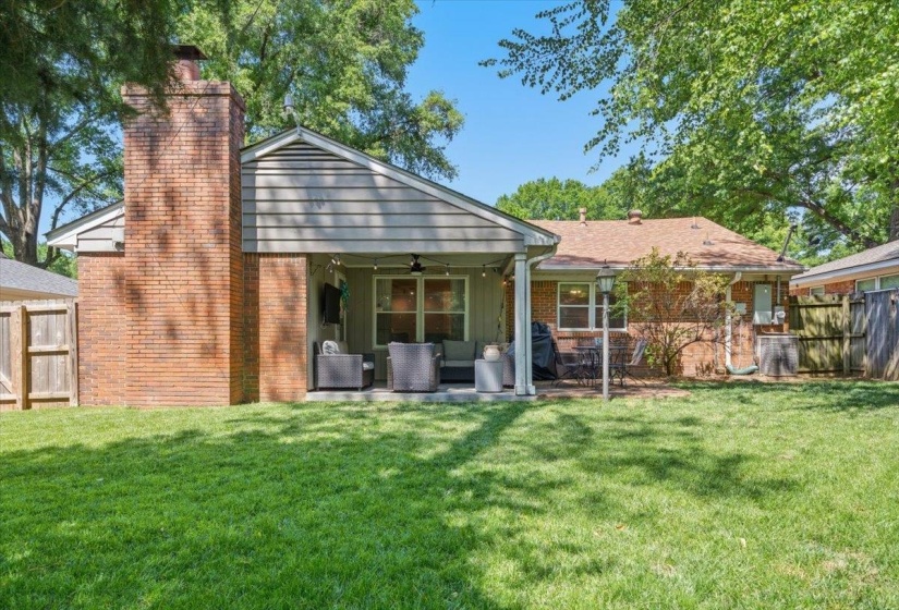 Expansive backyard featuring a brick chimney, a covered patio area with a ceiling fan, and a concrete patio