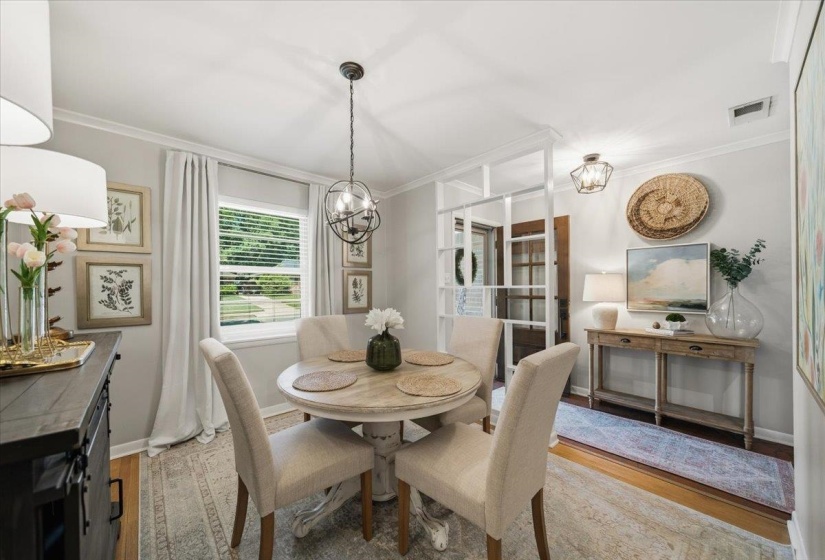 Dining area featuring a circular light wood-finish table with upholstered chairs, a window with blinds, and a built-in room divider with a white frame